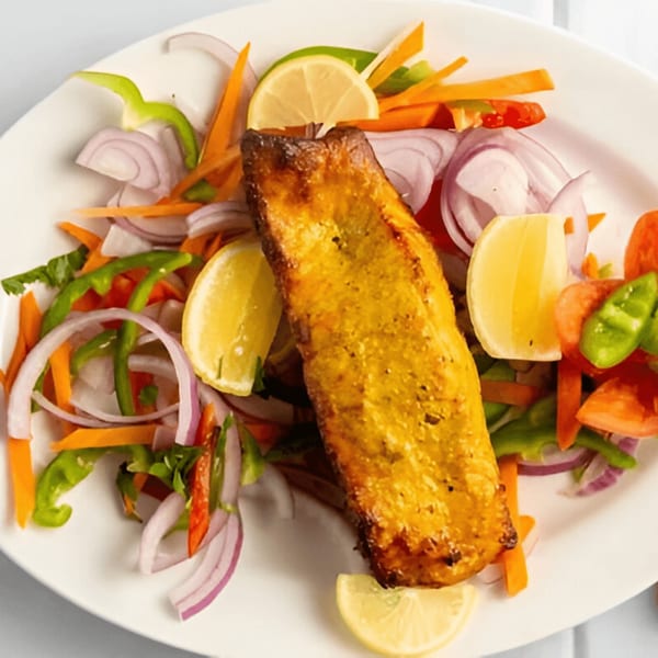 Mehfil Indian Restaurant's grilled fish, garnished with fresh onions, bell peppers, carrots, and lemon slices.