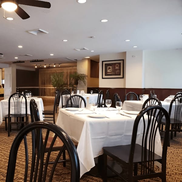 Dining room at Mehfil Indian Restaurant with white-clothed tables, dark chairs, and warm lighting.