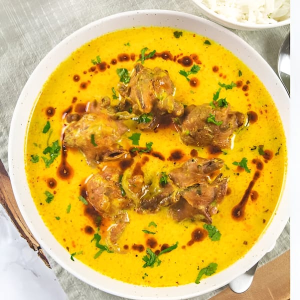 Close-up of a vibrant yellow Indian curry with meat pieces, garnished with fresh cilantro and oil.