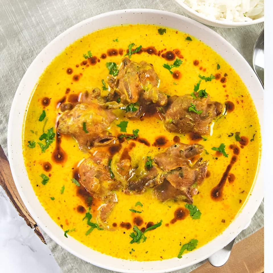 Close-up of a vibrant yellow Indian curry with meat pieces, garnished with fresh cilantro and oil.