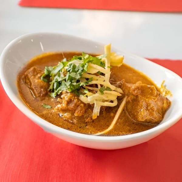 A white bowl of Mehfil Indian Restaurant's chicken curry, garnished with fresh cilantro and ginger.