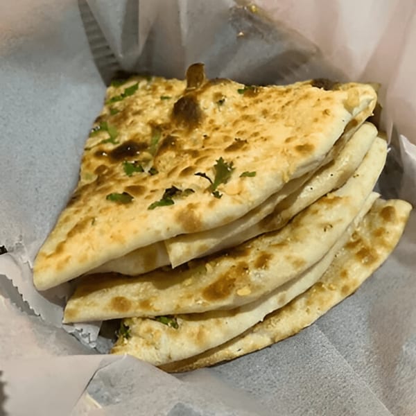 Stack of golden-brown Indian naan bread with green herbs, served in a white paper-lined basket.