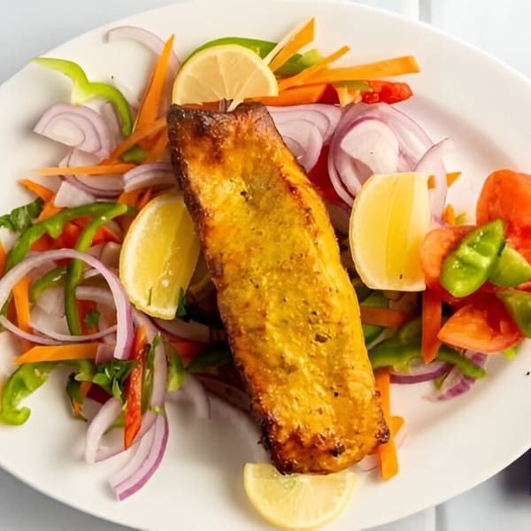 Indian grilled fish, garnished with lemon slices, red onions, bell peppers, and carrots.